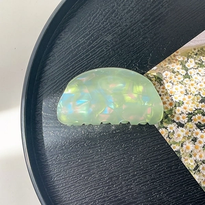 Macro detail of the light green iridescent crescent hair claw clip on a black tray