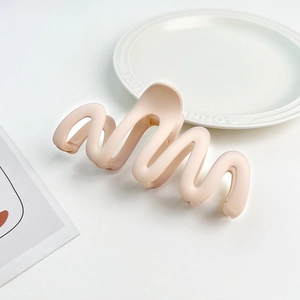 Detail shot of a matte light pink wavy hair claw clip on an elegant white ceramic plate