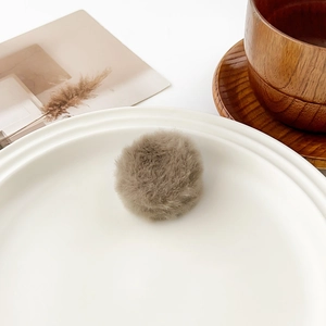 Close-up of soft camel plush pom-pom hair clip on elegant white ceramic plate decor