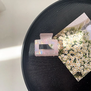 Detail of a square acrylic shark hair claw clip in pearlescent pink on a black tray