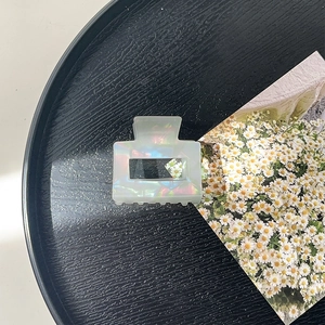 Detailed macro view of an iridescent white square hollow hair claw clip on black tray