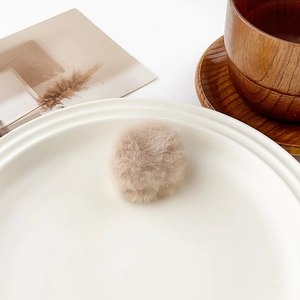 Detailed view of a soft beige plush hair clip accessory on a white decorative plate
