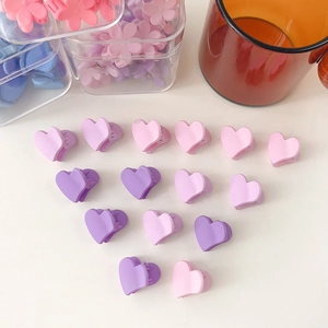 Vue macro de mini pinces à cheveux cœur colorées aux tons macaron mats sur fond blanc