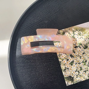 Detail view of large iridescent pink rectangular hair claw clip on black textured tray