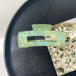Macro detail of large translucent aurora green acrylic hair claw clip on black tray