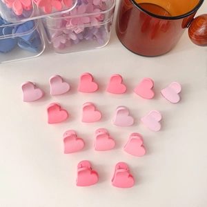 Détail macro de 15 mini-pinces à cheveux en forme de cœur rose dégradé sur table
