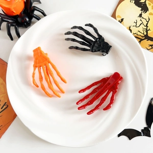 Barrettes main de squelette d'Halloween en noir, orange et rouge sur une assiette blanche