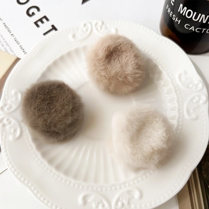 Three plush faux fur hair pom-poms in brown, tan, and cream on a vintage ceramic plate
