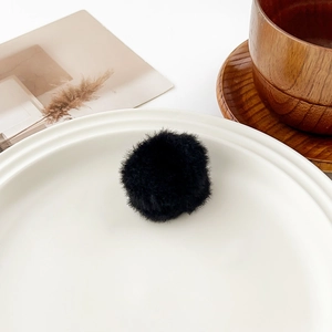 Close-up of soft black plush pom-pom hair clip on a minimalist white ceramic plate