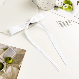 Detail of elegant white long ribbon bow hair clip in silky satin on decorative tray