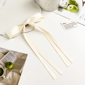 Detail of cream silk satin bow hair clip with long streamers on a white modern surface