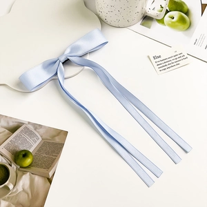 Detail view of light blue satin bow hair clip with long ribbons on a white desktop