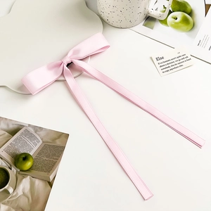 Detail of light pink satin bow hair clip with long flowing ribbons on white table