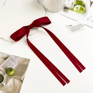 Detail of elegant deep burgundy satin bow hair clip with long flowing ribbons on desk