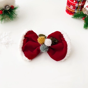 Detailed close-up of a festive red velvet Christmas bow hair clip with white plush trim and pompons