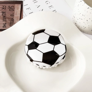 Detalle de una pinza de pelo acrílica con diseño de balón de fútbol en un plato blanco