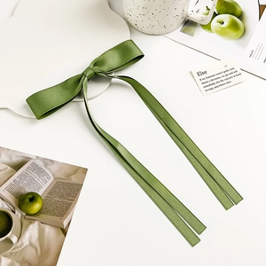 Detail shot of a soft green satin bow hair clip with elegant long ribbons on white surface