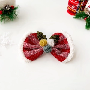 Detail of a sparkling red Christmas bow hair clip with white fleece trim and green holly leaves