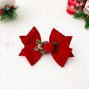 Detail of red velvet Christmas bow hair clip with a gold bell and festive green leaf décor