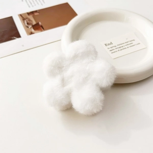 Dettaglio della pinza per capelli a fiore di peluche bianco su un tavolo bianco minimal