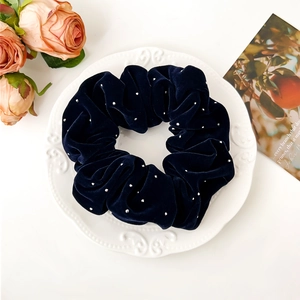 Détail d'un chouchou en velours bleu marine avec strass posé sur une assiette en porcelaine