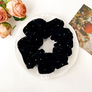 Détail d'un chouchou en velours noir avec strass sur un plateau blanc décoré