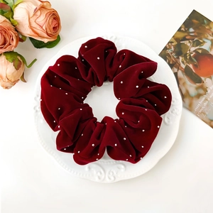 Détail d'un chouchou en velours bordeaux avec perles blanches sur une assiette en porcelaine