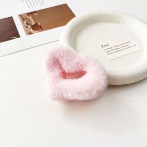 Dettaglio macro della molletta per capelli a cuore in peluche rosa su sfondo bianco
