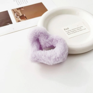 Dettaglio di una morbida molletta per capelli in peluche viola a cuore su vassoio bianco
