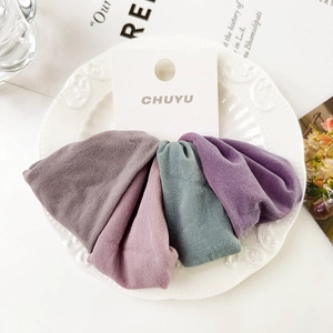 Detail of four wide elastic hair scrunchies in muted tones on a white branded card