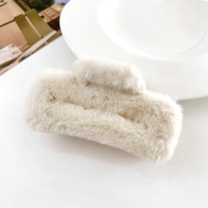 Detailed close-up of a large cream-white plush hair claw clip on a minimalist white surface
