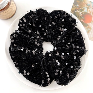 Detail of elegant black velvet scrunchie with sequins on a white decorative plate