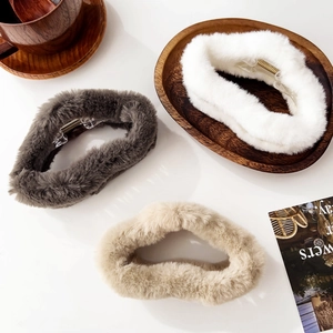 Three plush hair claws in grey, white, and beige on a wooden tray for winter styling
