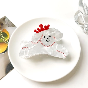 Detalle de pinza de pelo de caniche blanco con corona roja sobre plato de porcelana blanco