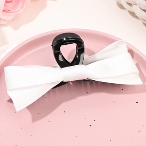 Détail d'une pince à cheveux avec nœud en ruban blanc posée sur une assiette décorative