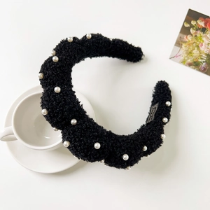 Macro detail of plush black faux fur headband with white pearl accents and handmade tag