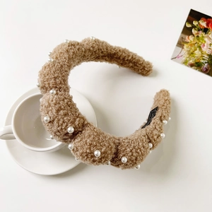 Close-up of plush coffee-brown wavy headband with white pearls on elegant white setting