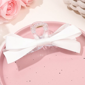 Détail d'une grande pince à cheveux avec nœud en ruban blanc sur un plateau rose