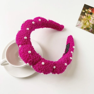Detail of rose red fuzzy headband with white faux pearls and handmade label on white background