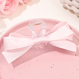 Détail d'une pince à cheveux à nœud en satin rose sur un plateau en céramique