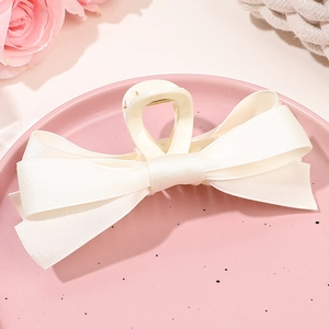Vue détaillée d'une pince à cheveux à double nœud crème sur un plateau décoratif rose