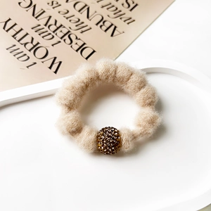 Detail of a plush beige hair tie featuring a knit texture and sparkling rhinestone bead