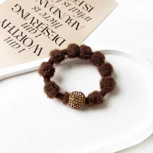 Close-up of brown plush hair tie with rhinestone gold bead on elegant white tray