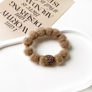 Detail of light brown plush scrunchie with a gold rhinestone ball on a minimalist tray