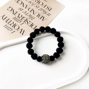 Close-up of black braided bracelet featuring a sparkling pavé crystal bead on white tray