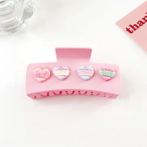 Détail d'une pince à cheveux rose mat avec gaufrage de cœurs LOVE colorés sur fond blanc