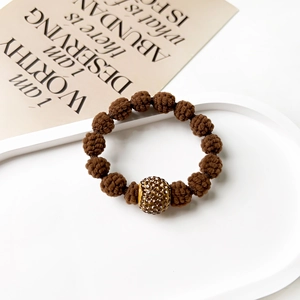 Detail view of brown woven hair tie with a crystal-encrusted gold bead on a display tray