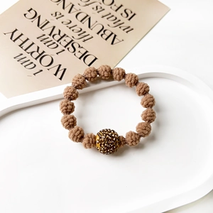 Close-up of brown woven hair tie with a gold pavé crystal bead on minimalist background