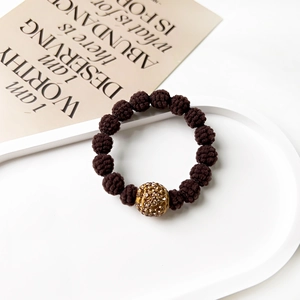 Detail view of brown knit beads and a gold sparkling rhinestone bead on a white tray