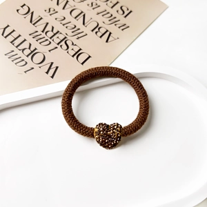 Detailed macro view of a brown knit scrunchie featuring a luxury rhinestone heart charm